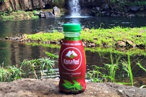 Kona Red Juice Bottle of KonaRed on a rock in front of a stream